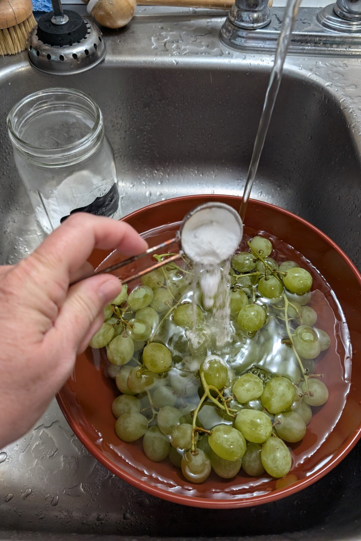 Χέρι χύνοντας σόδα ψησίματος σε ένα μπολ γεμάτο με σταφύλια και νερό